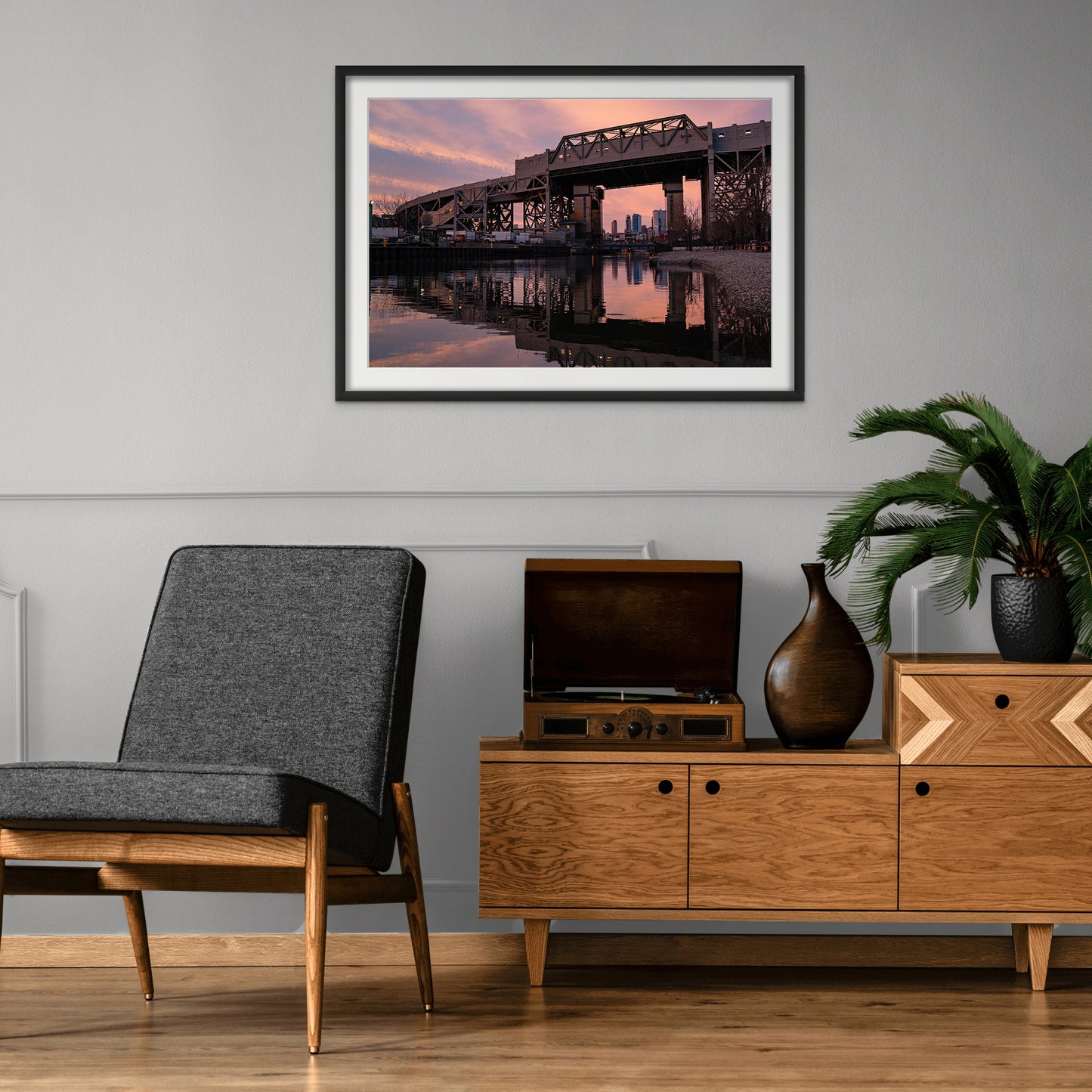A framed print of sunset behind the Smith & 9th St. subway station viaduct in Gowanus, Brooklyn is hung above a comfortable chair and an open record player.